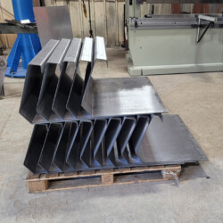 Stacked metal brackets on a wooden pallet in a workshop.
