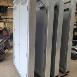 Four industrial steel double doors standing upright on a pallet in a workshop.