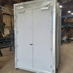 A set of double gray metal doors in a heavy-duty steel frame standing in a workshop.