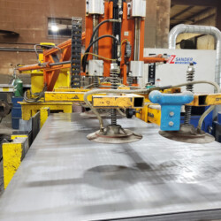 Industrial vacuum lifting machine positioning a large metal sheet on a workspace.