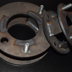 Two metal wheel spacer adapters with threaded bolts and welded supports.
