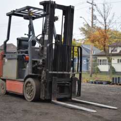 A Toyota forklift parked on a gravel lot in front of houses.