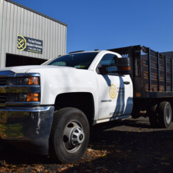 White Chevrolet 3500 HD dump truck parked in front of a Pro Tech Precision Machine and Fabrication building.