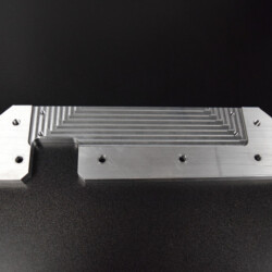 A machined metal bracket with a grooved surface and four mounting holes.