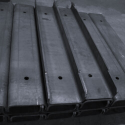 Stack of gray steel channel beams with pre-drilled holes.