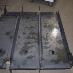 A rectangular metal plate with three sections and circular cutouts, lying on a concrete floor.