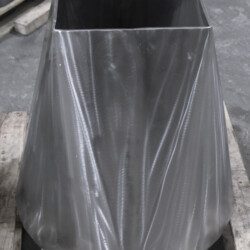 A metal conical transition piece with a rectangular top opening, resting on a wooden pallet.