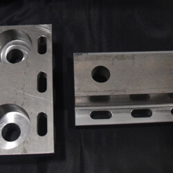 Two machined metal brackets with slotted mounting holes and circular cutouts on a dark background.