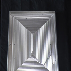 Rectangular metal plate with an engraved pattern of nested concentric rectangles and small mounting holes.