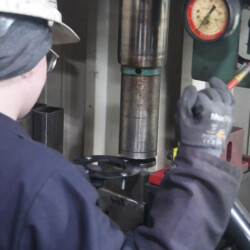 A worker in a hard hat and gloves operates an industrial hydraulic press.