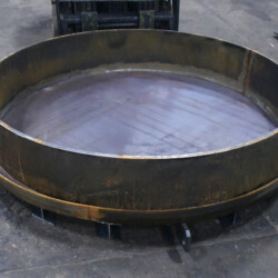 A large, circular metal industrial component with a rimmed base resting on a concrete floor.