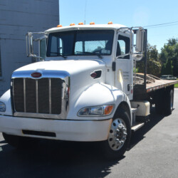 White Peterbilt flatbed truck parked on an asphalt lot.