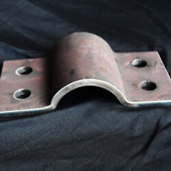 A flat steel mounting bracket with a central arched bridge and four bolt holes.