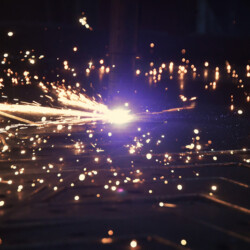 A plasma cutter slicing through metal plate, throwing off a spray of bright sparks.