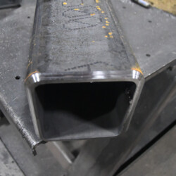 A square steel tube resting on a metal workbench.